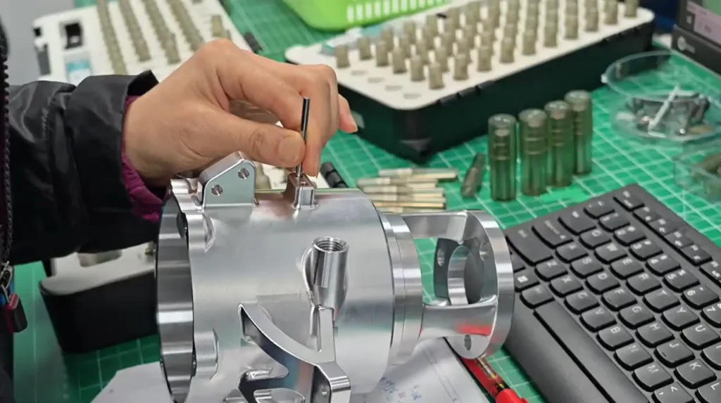 Engineer using pin gauges to inspect tight tolerances on a precision CNC machined aluminum wheel hub housing in a manufacturing workshop.